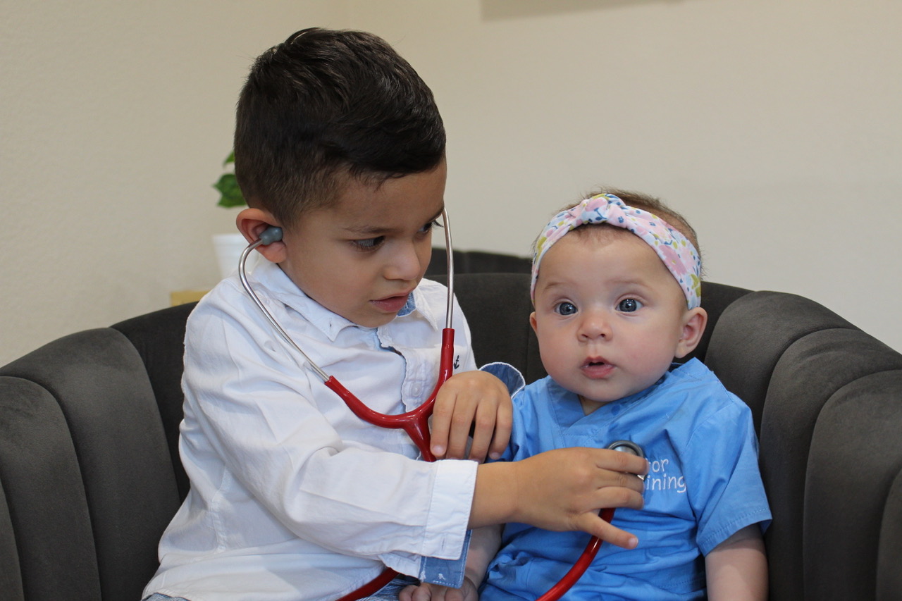 A young boy holds a stethoscope to a baby’s chest